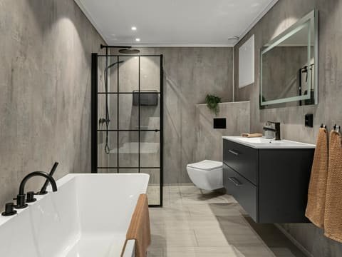 Salle de bains rénovée : baignoire îlot, douche à verrière noire, murs gris effet béton et meuble vasque sombre