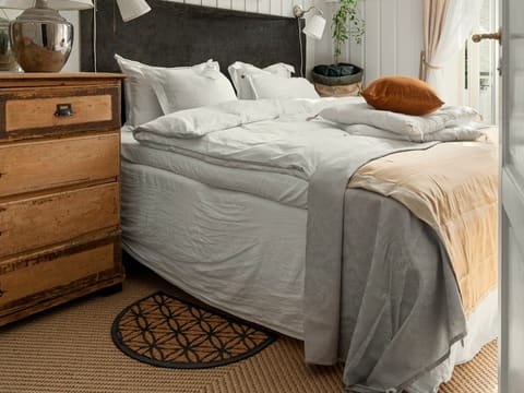Chambre rénovée aux murs lambrissés peints en blanc, lit au linge clair et commode ancienne en bois