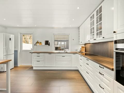 Cuisine rénovée en L : façades blanches à cadre, plan de travail en bois, crédence sombre et sol en bois