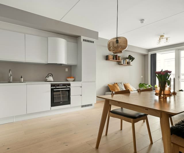 Cuisine rénovée ouverte sur la salle à manger : façades blanches, table en bois, parquet clair et lumière naturelle