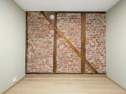 Séjour vide après travaux : mur en briques et pans de bois apparents, murs blancs, parquet en chêne clair